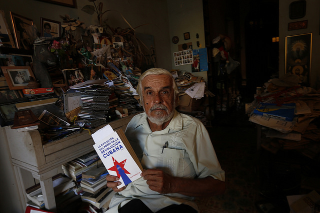 Enrique López Oliva, un periodista jubilado y profesor en activo, muestra la portada de un libro dentro de su estudio en el municipio Playa, uno de los que conforman la capital de Cuba. Crédito: Jorge Luis Baños/IPS