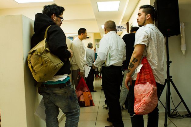 Como parte del proceso de ingreso al país, los deportados deben pasar por varias entrevistas y también tienen a su disposición un servicio de atención médica, para aquellos que lo deseen, como los que esperan en esta fila ante el consultorio del Centro de San Salvador. Crédito: Edgardo Ayala/IPS