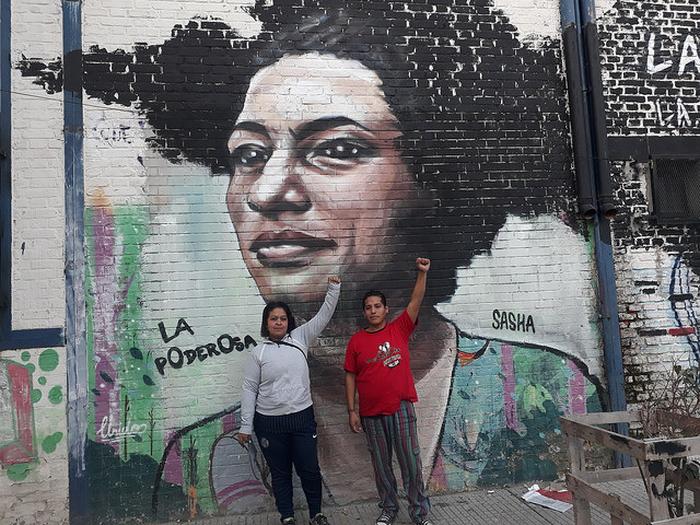 Lucy Mercado y Marcos Basualdo, dos integrantes de la organización social de La Poderosa, posan delante de un mural en la Villa 21, un barrio precario de Buenos Aires, que homenajea a Marielle Franco, la política y activista de derechos humanos brasileña que fue asesinada en marzo en Río de Janeiro. Crédito: Daniel Gutman/IPS