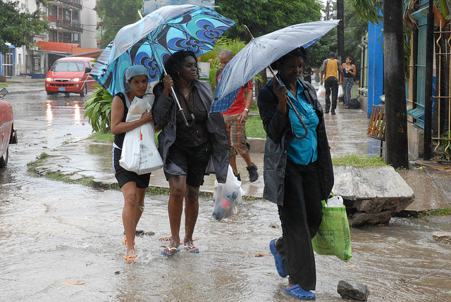 Varias mujeres caminan en medio de la lluvia hacia sus hogares provistas con víveres, como parte de sus previsiones ante la inminente llegada a Cuba del huracán Gustav, en 2008, en un barrio de La Habana. Crédito: Jorge Luis Baños/IPS
