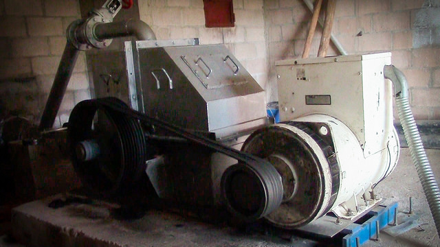 El pequeño generador, en la sala de máquinas construida por los vecinos de Joya de Talchiga. Los hombres del caserío cargaron, con maderos en sus hombros, la pesada turbina que mueve el generador de 58 kW, ya que no hay acceso a vehículos donde se instaló la maquinaria de la Minicentral Hidroeléctrica El Calambre, en el montañoso municipio de Parquín, en el este de El Salvador. Crédito: Edgardo Ayala/IPS