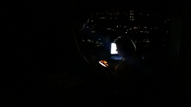 Algunas luces en barrios lejanos, a los que ya había llegado la electricidad, y algo de batería en los dispositivos animan la búsqueda de información sobre los familiares distantes en un hogar de Colinas de Santa Mónica, en una colina de Caracas, durante el inédito apagón de Venezuela. Crédito: Humberto Márquez/IPS