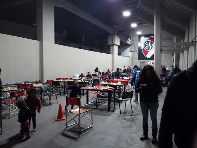 Algunos acogidos en las tribunas del mayor estadio de fútbol argentino, el River Plate, alargan la sobremesa tras cenar caliente, antes de dormir en sus instalaciones, dentro del aporte solidario de los clubes deportivos de Buenos Aires para apoyar a la población sin techo ante la primera ola de frío del invierno austral. Crédito: Daniel Gutman/IPS