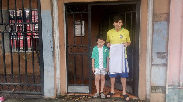 Vílber Menjívar, junto a su hijo Dylan, de 7 años, fuera de su vivienda, en el noreste de San Salvador, con su bandera blanca entre las manos. Este camarero se quedó sin empleo cuando comenzó el confinamiento, establecido por el presidente Nayib Bukele para reducir el contagio de covid-19 y tuvo que vender su lavadora por 100 dólares para alimentar a su pequeño. Ahora que desde este 15 de junio, comenzó la paulatina apertura de actividades, espera poder volver a trabajar. Foto: Edgardo Ayala/IPS